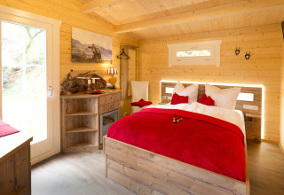 Cozy glamping cabin with wooden interior, double bed and red accents at Campingpark Wiesenbeker Teich.