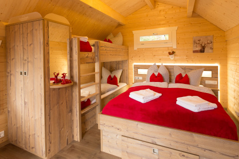 Knusse glampinghut bij Campingpark Wiesenbeker Teich met houten stapelbedden, rood textiel en gezellig interieur.
