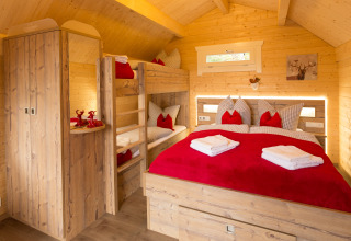 Cozy glamping cabin at Campingpark Wiesenbeker Teich featuring wooden bunk beds, red bedding, and rustic charm.