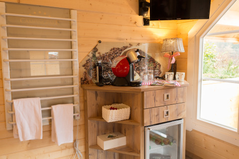 Innenraum einer Glamping-Unterkunft mit Kaffeemaschine, Minibar, Holzregal und gemütlicher Dekoration.