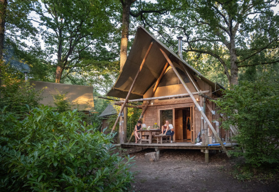 Glamping accommodatie bij Huttopia Rambouillet - Glamping île de France, twee mensen op de veranda in het bos.