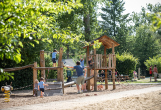 Bambini giocano in un parco giochi in legno a Huttopia Rambouillet - Glamping île de France immerso tra gli alberi.