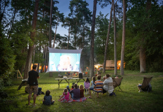 Cinema all'aperto nella foresta a Huttopia Rambouillet - Glamping île de France, persone guardano un film insieme.