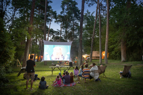 Buitenbioscoop bij Huttopia Rambouillet - Glamping île de France, mensen kijken samen een film in het bos.