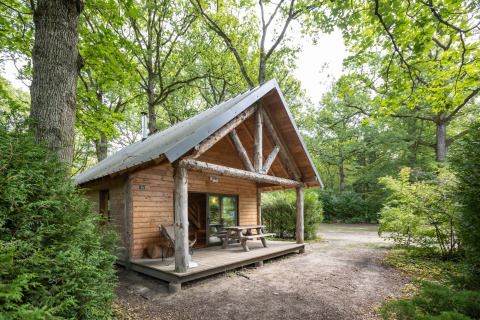 Wooden glamping cabin at Huttopia Rambouillet - Glamping île de France, surrounded by lush green forest.