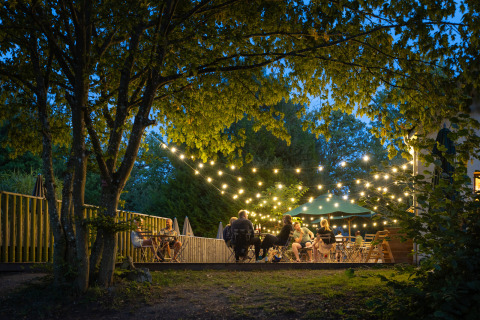 Soirée en plein air à Huttopia Rambouillet Glamping Île-de-France avec des personnes sous guirlandes lumineuses.