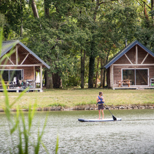 Twee houten hutten aan het meer bij Village Huttopia Lac de Rillé Glamping Val de Loire, persoon op supboard.