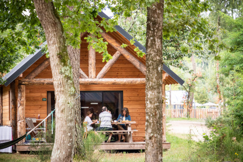 Eine Familie frühstückt auf der Veranda einer Holzhütte im Village Huttopia Lac de Rillé - Glamping Val de Loire.