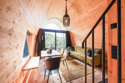 Luksuriøst glamping-hytteinteriør med moderne indretning og store vinduer med udsigt over skov i Vorarlberg.