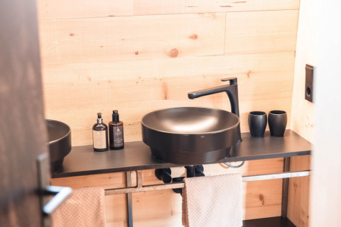 Baño moderno con lavabo negro y pared de madera en chalet de lujo Alpencamping Nenzing en Vorarlberg.