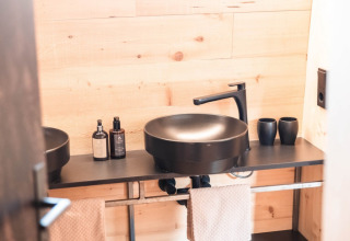 Bagno moderno con lavabo nero e parete in legno nello chalet di lusso Alpencamping Nenzing in Vorarlberg.