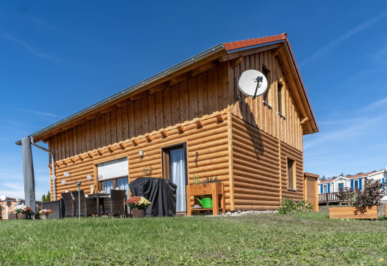 Houten lodge op Camping & Vakantiepark Orsingen - Landhuis Baden-Württemberg, onder een helder blauwe lucht.