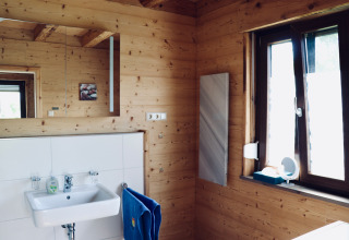 Baño en una cabaña de madera en Camping & Vakantiepark Orsingen - Landhuis Baden-Württemberg, con lavabo y ventana.