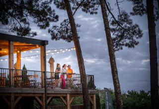 Fire personer står på terrassen på Camping Huttopia Arcachon - Glamping Nouvelle-Aquitaine omgivet af træer.