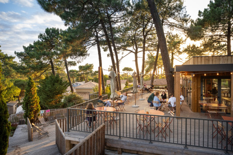 Terrasse en plein air du Camping Huttopia Arcachon, entourée de pins et de vacanciers en soirée.