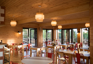 Sala da pranzo interna con arredi in legno e sedie rosse al Camping Huttopia Arcachon, Glamping Nouvelle-Aquitaine.