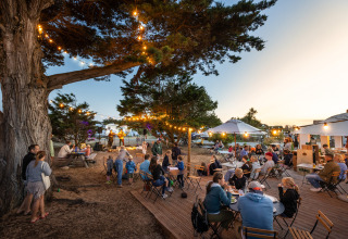 Evening at Huttopia Ars-en-Ré Glamping in Nouvelle-Aquitaine, people dining, string lights and trees.