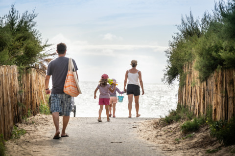 Familie geht am Huttopia Ars-en-Ré – Glamping Nouvelle-Aquitaine auf einem Weg zum Strand in der Sonne.