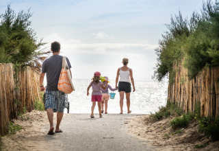 Familia camina hacia la playa en Huttopia Ars-en-Ré – Glamping Nouvelle-Aquitaine, rodeados de vegetación.