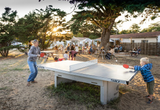 Enfants et adultes jouent au tennis de table en plein air à Huttopia Ars-en-Ré, glamping en Nouvelle-Aquitaine.