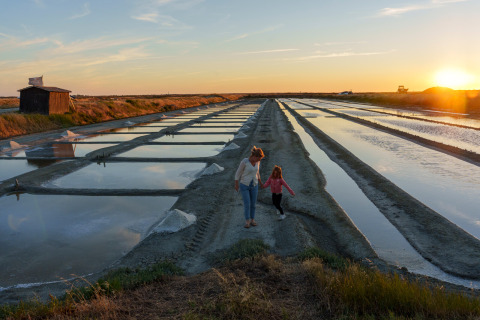 Madre e figlia passeggiano al tramonto tra le saline vicino a Huttopia Ars-en-Ré – Glamping Nouvelle-Aquitaine.