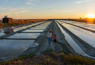 Madre e hija caminan junto a las salinas al atardecer cerca de Huttopia Ars-en-Ré – Glamping Nouvelle-Aquitaine.