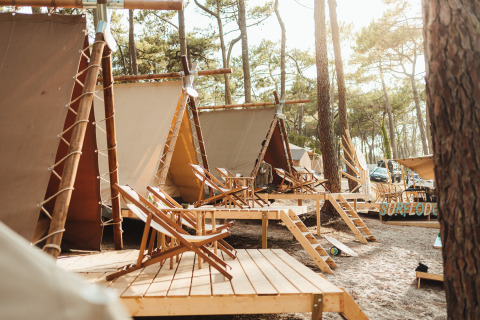 Glamping-Zelte im Wald bei Enter the wave – Forestcamp Biscarrosse mit Holzterrassen und Liegestühlen.