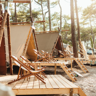 Glamping tents at Enter the wave – Forestcamp Biscarrosse, set amid pine trees with deck chairs on wooden terraces.
