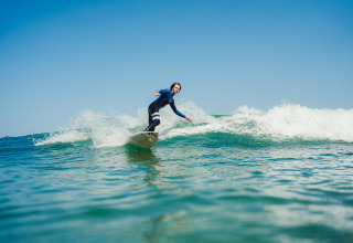 Surfer nyder bølgerne under en blå himmel nær Forestcamp Biscarrosse, ideel til glamping og camping.