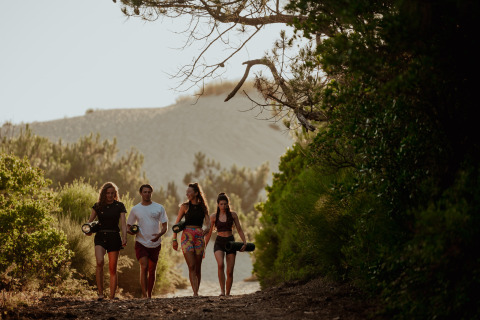 Cuatro personas caminan por un sendero forestal en Enter the wave – Forestcamp Biscarrosse, rodeados de naturaleza.
