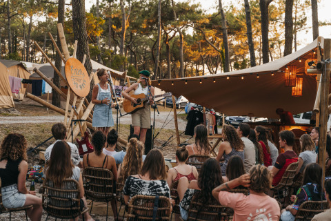Outdoor musical performance among tents and trees at 'Enter the Wave – Forestcamp Biscarrosse' glamping site.