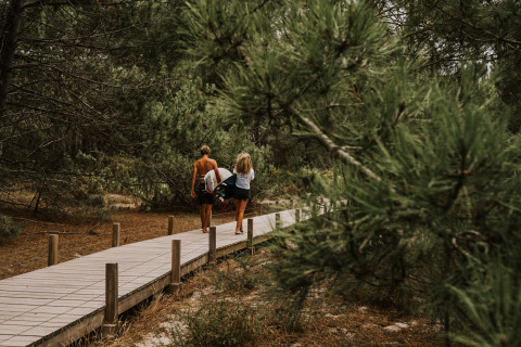 Zwei Personen mit Surfbrettern spazieren auf dem Waldweg im Enter the wave – Forestcamp Biscarrosse.