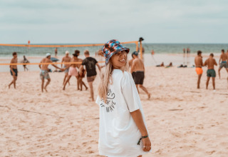 Vrouw met witte t-shirt en hoedje lacht op het strand bij glamping Enter the wave – Forestcamp Biscarrosse.