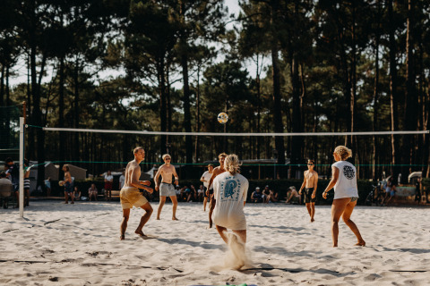 Junge Leute spielen Beachvolleyball bei Sonne auf Enter the wave – Forestcamp Biscarrosse, Wälder im Hintergrund.
