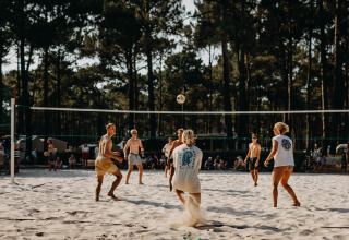 Des jeunes jouent au volley de plage au Enter the wave – Forestcamp Biscarrosse, entourés de forêt.
