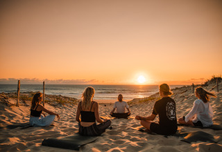 Grupo practicando yoga juntos en la playa al atardecer en Forestcamp Biscarrosse, sitio de glamping.