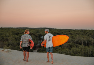 Due surfisti camminano tra le dune al tramonto vicino al glamping Forestcamp Biscarrosse, portando le tavole.