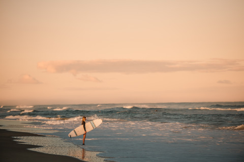 Surfer met een plank op het strand bij zonsondergang aan Forestcamp Biscarrosse, ideaal glampen.