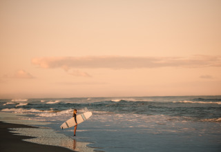 Surfer am Strand mit Surfbrett bei Sonnenuntergang nahe Forestcamp Biscarrosse, ideal zum Glamping.