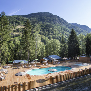 Wooden terrace with swimming pool and loungers in the scenic mountains at Huttopia Vanoise – Bozel, Glamping Savoie.