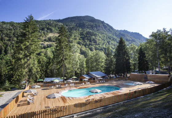 Terrazza in legno con piscina e lettini nella natura montuosa presso Huttopia Vanoise – Bozel, Glamping Savoie.