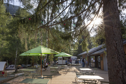 Terrazza esterna con ombrelloni verdi e tavoli presso Huttopia Vanoise – Bozel – Glamping Savoie.