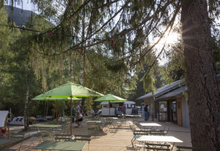 Buitenterras met groene parasols en tafels bij Huttopia Vanoise – Bozel – Glamping Savoie camping.