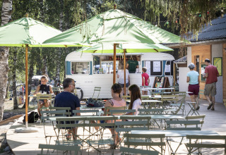 Zona pranzo all'aperto con ombrelloni verdi e persone davanti a un food truck a Huttopia Vanoise – Bozel, Glamping Savoie.