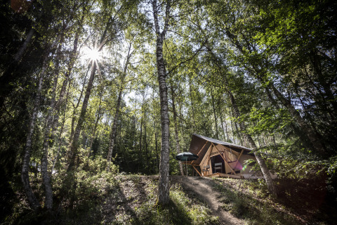Alojamiento glamping Huttopia Vanoise – Bozel – Glamping Savoie rodeado de árboles y luz solar en el bosque.