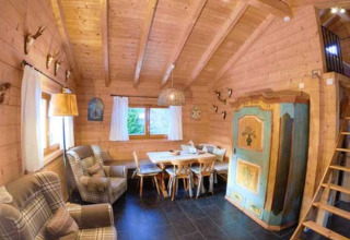 Interno di una confortevole baita di legno con poltrone, zona pranzo e armadio dipinto a Natur-Camping Langenwald.