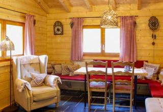 Interno accogliente di una baita in legno con angolo pranzo, cuscini morbidi e atmosfera rustica.