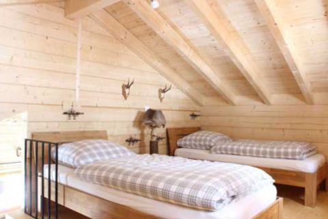 Alojamiento glamping de madera con dos camas individuales y vigas inclinadas en Natur-Camping Langenwald.