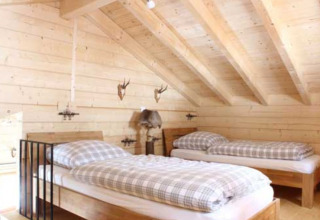 Hébergement glamping en bois avec deux lits simples et poutres inclinées au Natur-Camping Langenwald.
