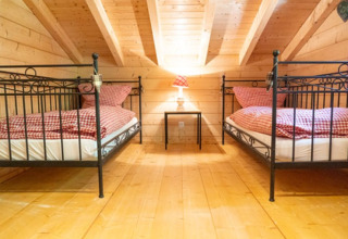 Glampingaccommodatie met twee eenpersoonsbedden, houten interieur en geruite lakens bij Natur-Camping Langenwald.